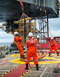 Offshore workers handling equipment on a vessel near an offshore platform.